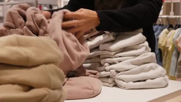 Närbild av kvinnliga händer som går igenom högen av vikta pastell färg hoodies letar efter perfekt storlek — Stockvideo