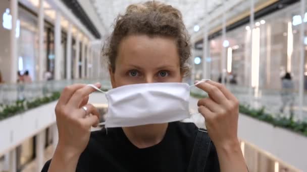 Retrato de mulher jovem colocando máscara facial em olhar direto para a câmera. Limitações nos espaços públicos durante a pandemia de covid-19. — Vídeo de Stock