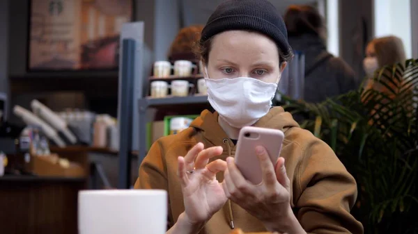 Бизнес в общественных местах на фоне вспышки ковида-19. Женщина в кафе снимает маску для лица, чтобы выпить кофе с яблочным пирогом, читая последние новости в Интернете. — стоковое фото