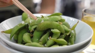 Çubuklar kaseden edamame fasulyesi topluyor. Öğle yemeği için Japon atıştırmalıkları. Sağlıklı Asya mutfağı.