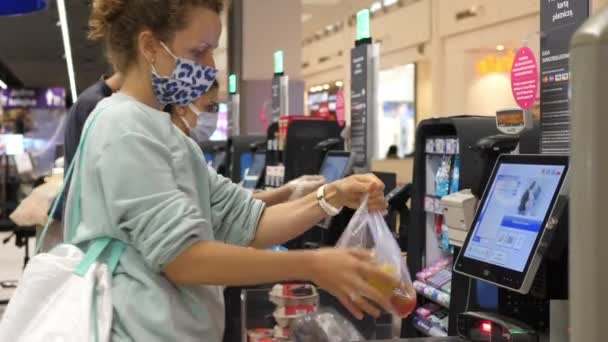Bevásárlás a covid-19-es járvány idején. Kaukázusi lány arcmaszkban, önkijelentkezéssel egy szupermarketben. Varsó-Lengyelország-2020 — Stock videók