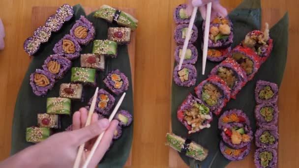 Vista superior de dos manos recogiendo rollos de sushi de bandejas de madera llenas de sushi. Colorida comida hipster de moda — Vídeos de Stock