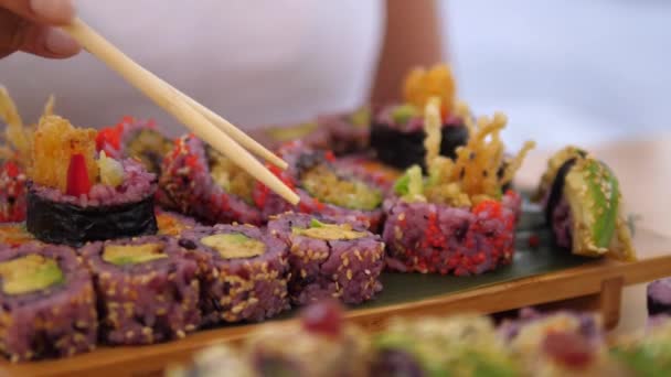 Mão escolhendo um rolo de sushi colorido com pauzinhos. Artesanato asiático conceito de comida de rua — Vídeo de Stock
