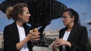 Friendship at workplace. Brunette business woman helps to clean the face of her blonde co-worker while having lunch outdoors. Healthy environment at workplace and teamwork 
