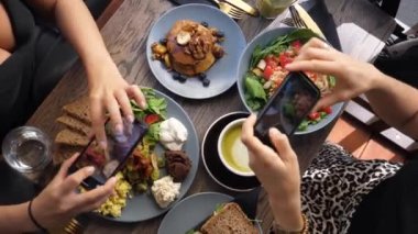 Renkli, sağlıklı bir brunch 'ın fotoğrafını çeken iki kişinin üst görüntüsü. 