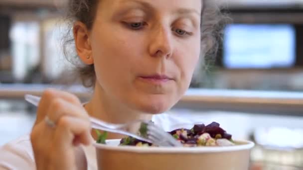 Голодна жінка їсть салат з великою кількістю листя, буряка та горіхів. Обід на продовольчому майданчику ТРЦ . — стокове відео