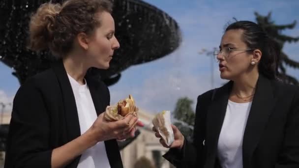 Blond en brunette collogues delen fast food maaltijd tijdens hun lunch buiten het kantoor. — Stockvideo