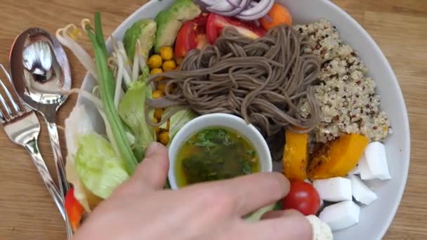 Ansicht von Hand, wie man Dressing auf warmen Salat mit Sobanudeln, Quinoa und frischem Gemüse gießt. Ausgewogene Ernährung und gesunder Lebensstil — Stockvideo