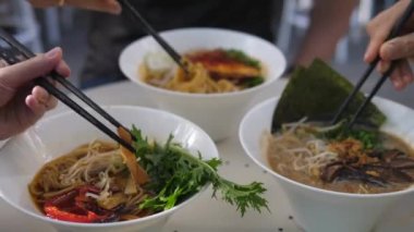 Vejetaryen Asya mutfağı. Ramen çorbasını çubuklarla karıştıran üç kişinin yan görüntüsü.