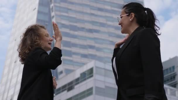 Deux femmes d'affaires se donnent un cinq haut et se joignent dans un câlin joyeux célébrant leur succès au travail devant les gratte-ciel — Video