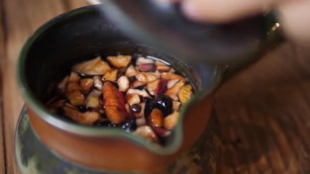 Du thé. La main ramasse le couvercle de la bouilloire à thé, remue la boisson avec une cuillère à café et montre les fruits secs à la caméra — Video