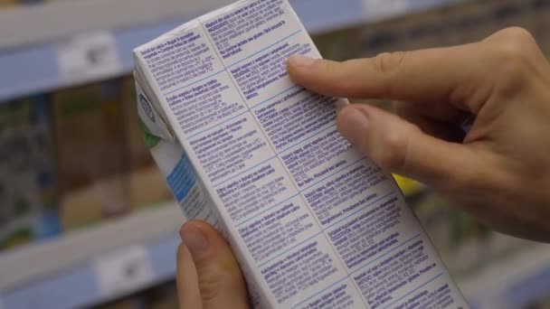 Close up de duas mãos segurando o produto em embalagem de papel para ler as informações do rótulo na loja. Conceito de compras consciente — Vídeo de Stock