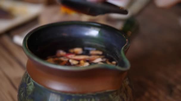 Zbliżenie mieszania gorącej herbaty w tradycyjnym dzbanku herbaty. Kwiaty i kawałki suchych owoców na łyżeczce. — Wideo stockowe