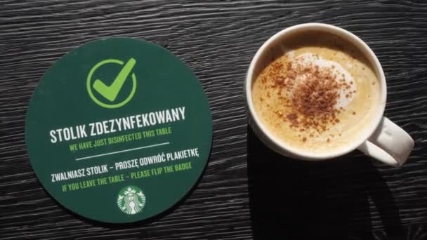 Top view of hand picking up mug with cappuccino from table with disinfection sign. Safety measures to prevent spread of corona virus in Starbucks. Warsaw - Poland- 2020 — Wideo stockowe