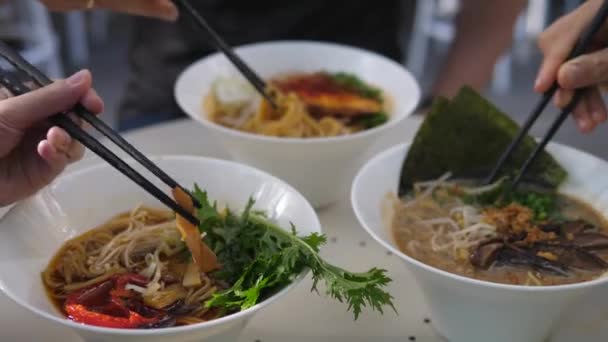 Cocina asiática vegana. Vista lateral de tres personas mezclando ingredientes en sopa de ramen con palillos — Vídeo de stock