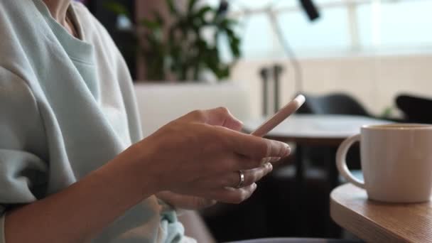 Close up of hands typing on smatphone in a coffee place.White porcelain mug on a wooden table — Stock Video