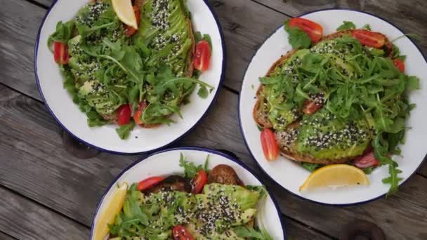 Bovenaanzicht van 3 borden avocado toast met groenten en sesam. Plantaardige voeding. — Stockvideo