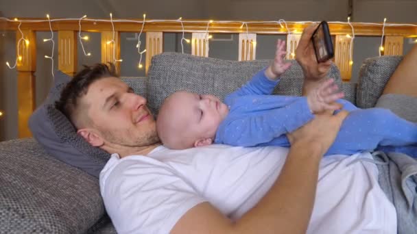 Pai feliz e bebê pequeno com smartphone tomando selfie em casa. — Vídeo de Stock