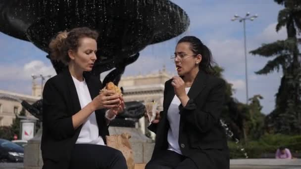 Обід розбивається на відкритому повітрі. Дві жінки-офіцери їдять фастфуд біля фонтану — стокове відео