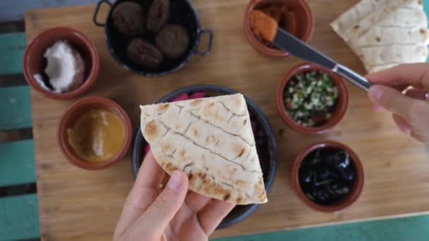 Draufsicht auf gesunde vegane Bio-Dips, Falafels, Essiggurken und Tabbouleh. Humus auf Pita verteilen. Köstliche israelische Küche. — Stockvideo