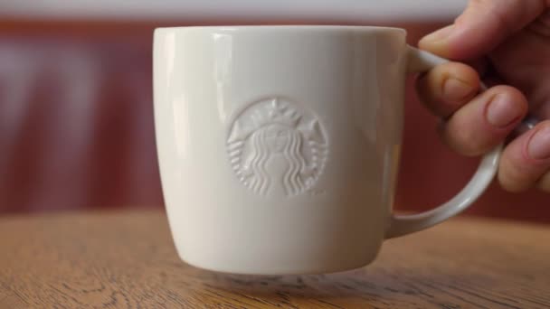Detailní záběr rukou dávat bílý šálek kávy Starbucks na dřevěný stůl. Objednávka kavárny. Varšava-Polsko-2020 — Stock video