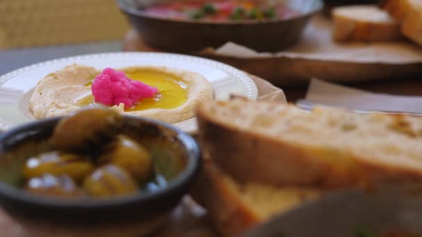 Shakshuka sartén caliente y hummus untado servido con aceitunas sobre tabla de madera. Almuerzo equilibrado a base de plantas en el restaurante vegano de Oriente Medio — Vídeos de Stock