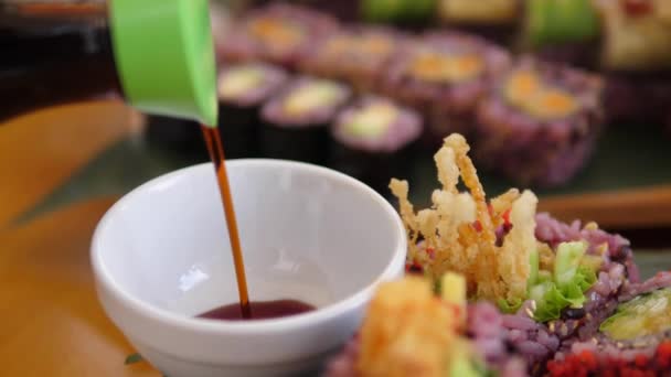 Sojasauce in weiße Porzellansauce gießen. Bunte vegane Sushi-Rollen auf Holztabletts — Stockvideo