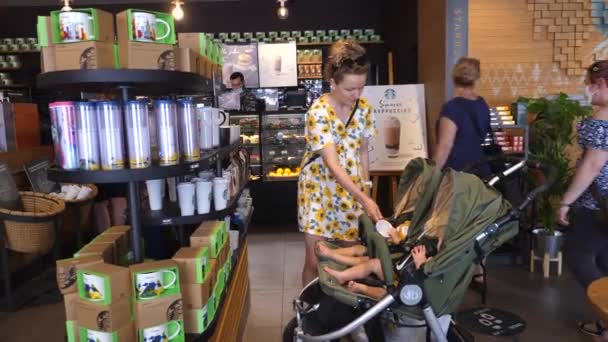 Młoda mama wybiera rzeczy z wyspy i bawi się bliźniaczkami w kawiarni Starbucks. Warszawa-Polska-2020 — Wideo stockowe