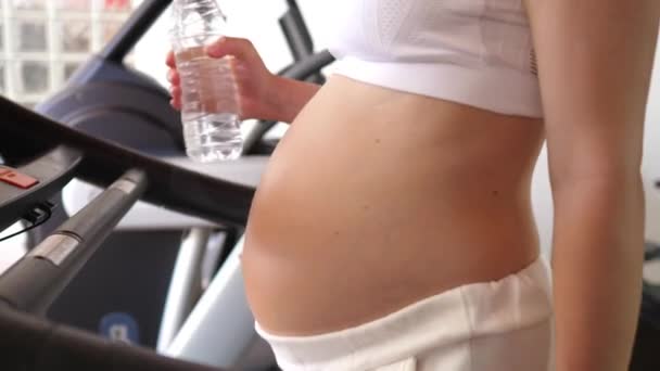 Mujer embarazada haciendo ejercicio en la cinta de correr con botella de agua en un gimnasio. — Vídeos de Stock