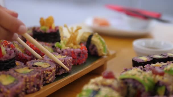 Vacsora a japán étteremben. Oldalsó nézet két kéz kezében színes sushi tekercs evőpálcikával. Kézműves keleti konyha koncepciója — Stock videók