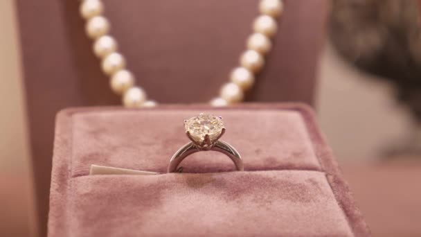 Кольцо с бриллиантом весом 4 карата в блестящей огранке выставлено на витрине роскошного ювелирного бутика. Жемчужное ожерелье на спине. — стоковое видео