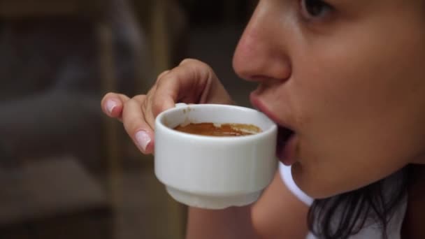 Primo piano della giovane donna che sorseggia un sorso di espresso fresco dalla tazza di porcellana bianca all'aperto. Cultura del caffè — Video Stock