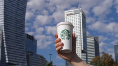 Beyaz eli Starbucks kahve fincanıyla modern binaların ve mavi gökyüzünün arka planına yakın tutun. Büyük şehirde bir kafe zinciri. Varşova-Polonya-2020.