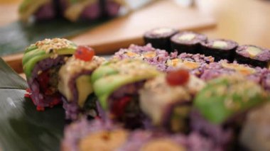 Bambu yaprakları üzerinde servis edilen rengarenk suşi rulolarının çeşitli türlerini kapat