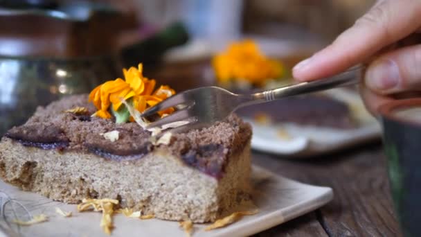 Κοντινό πλάνο του πιρουνιού σπάζοντας ένα κομμάτι ωμό κέικ vegan διακοσμημένο με λουλούδια. Τσάι κόμμα σε ρουστίκ στυλ — Αρχείο Βίντεο