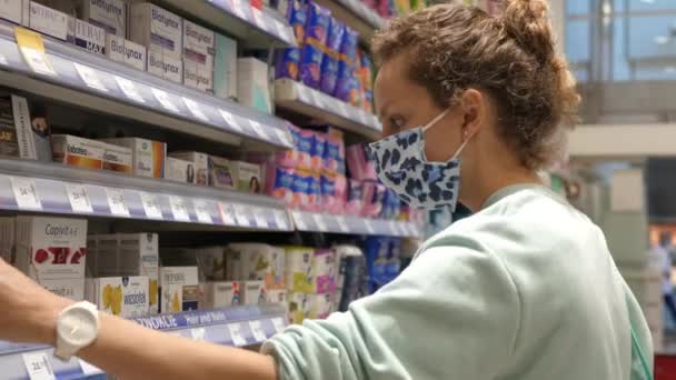 Mujer joven que usa mascarilla protectora elige pastillas en la farmacia. Varsovia-Polonia-2020 — Vídeos de Stock