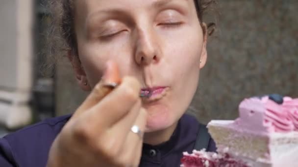 Chica hambrienta comiendo con alegría un pedazo de pastel de crema de bayas veganas en capas con glaseado rosa y arándanos. — Vídeos de Stock