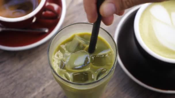 Vista superior de la mano revolviendo matcha té verde hielo con paja de plástico. Bebidas veganas refrescantes — Vídeos de Stock