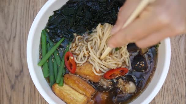 Cuisine asiatique biologique saine. Plan supérieur de baguettes cueillette de nouilles à partir de soupe de ramen épicée fraîche chaude. — Video
