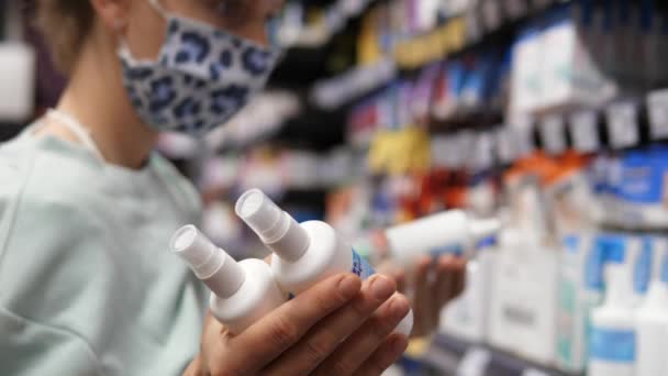 Крупным планом женщина в маске выбирает спрей в аптеке. Концепция здравоохранения — стоковое видео