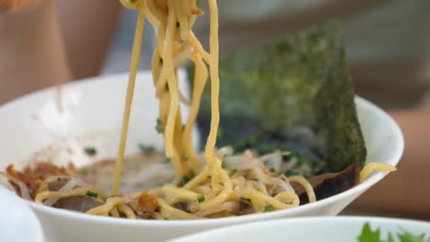 Trendig fet asiatisk gatumat. Närbild av nudlar från ram soppor hängande på ätpinnar. — Stockvideo