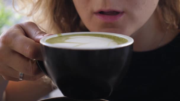 Blisko dziewczyny cieszącej się łykiem ciepłego cappuccino w czarnym kubku. Koncepcja sztuki latte — Wideo stockowe