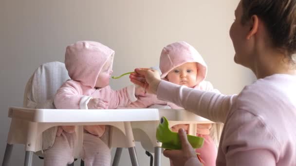 Ευτυχισμένη μητέρα που ταΐζει αστεία χαρούμενα δίδυμα μωρά από το κουτάλι. — Αρχείο Βίντεο