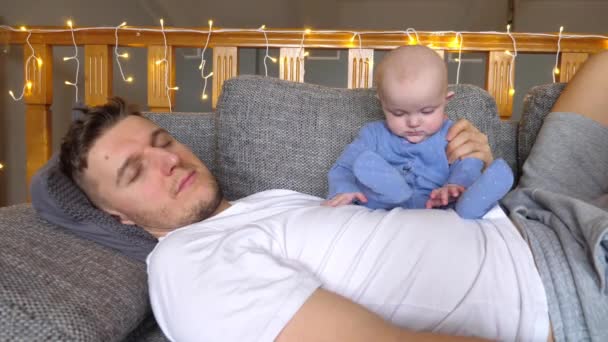 Zmęczony ojciec sypiający z wesołym dzieckiem — Wideo stockowe