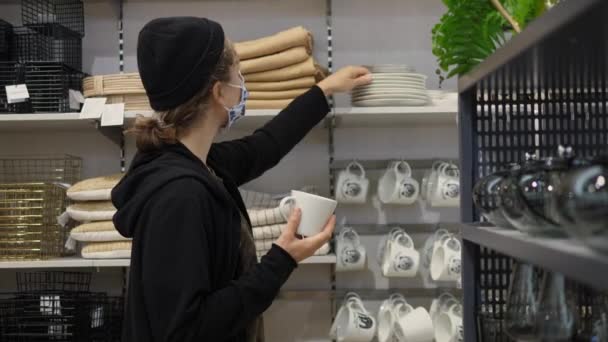 Jonge vrouw draagt beschermende gezichtsmasker kiest houten aardewerk in in dinneware afdeling van home decor winkel — Stockvideo