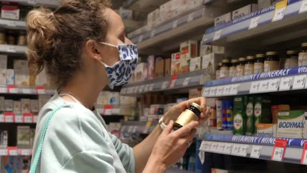 Sklep farmaceutyczny. Biała kobieta w masce do twarzy, wybierająca lekarstwa, czytająca etykiety na butelkach. Warszawa-Polska-2020 — Wideo stockowe