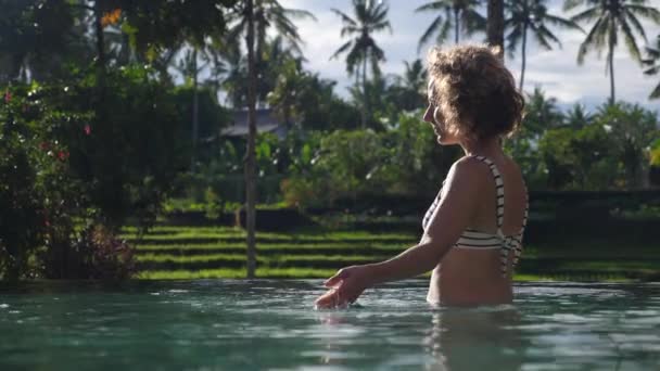 Una bella donna bionda in bikini che si rilassa in piscina. Paesaggio tropicale — Video Stock