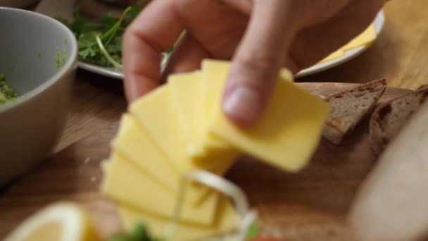 Vue latérale des mains organisant le petit déjeuner. Placer le fromage jaune sur du pain en bois.Petit déjeuner sain avec pain complet cuit à la maison dans un style rustique. — Video