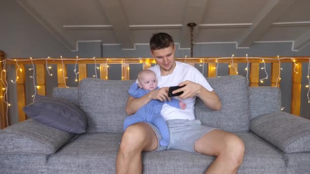 Πατέρας κρατώντας το μωρό και χρησιμοποιώντας έξυπνο τηλέφωνο στο σπίτι. — Αρχείο Βίντεο