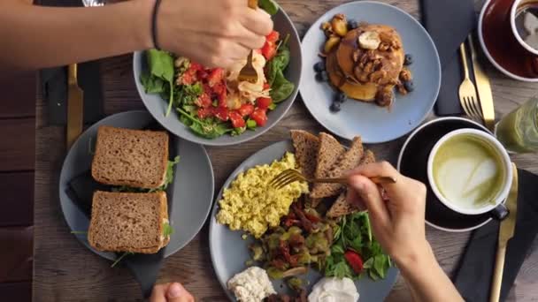 Tampilan atas tangan makan makanan organik vegetarian sehat sarapan lengkap Inggris, pasta salad dan pancake vegan disajikan di atas meja kayu — Stok Video